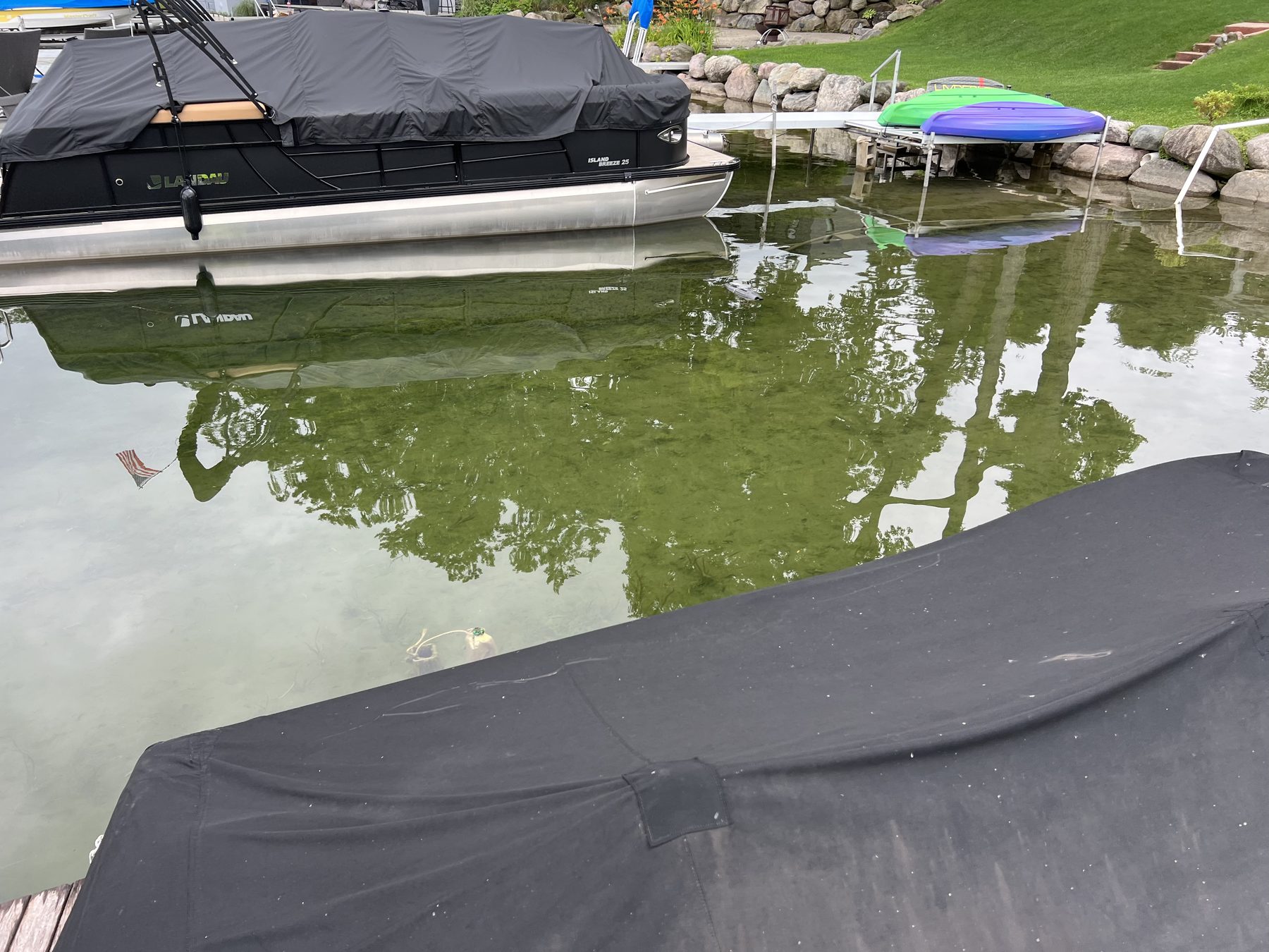 Covered pontoon and kayaks at a private shoreline with rock and grass