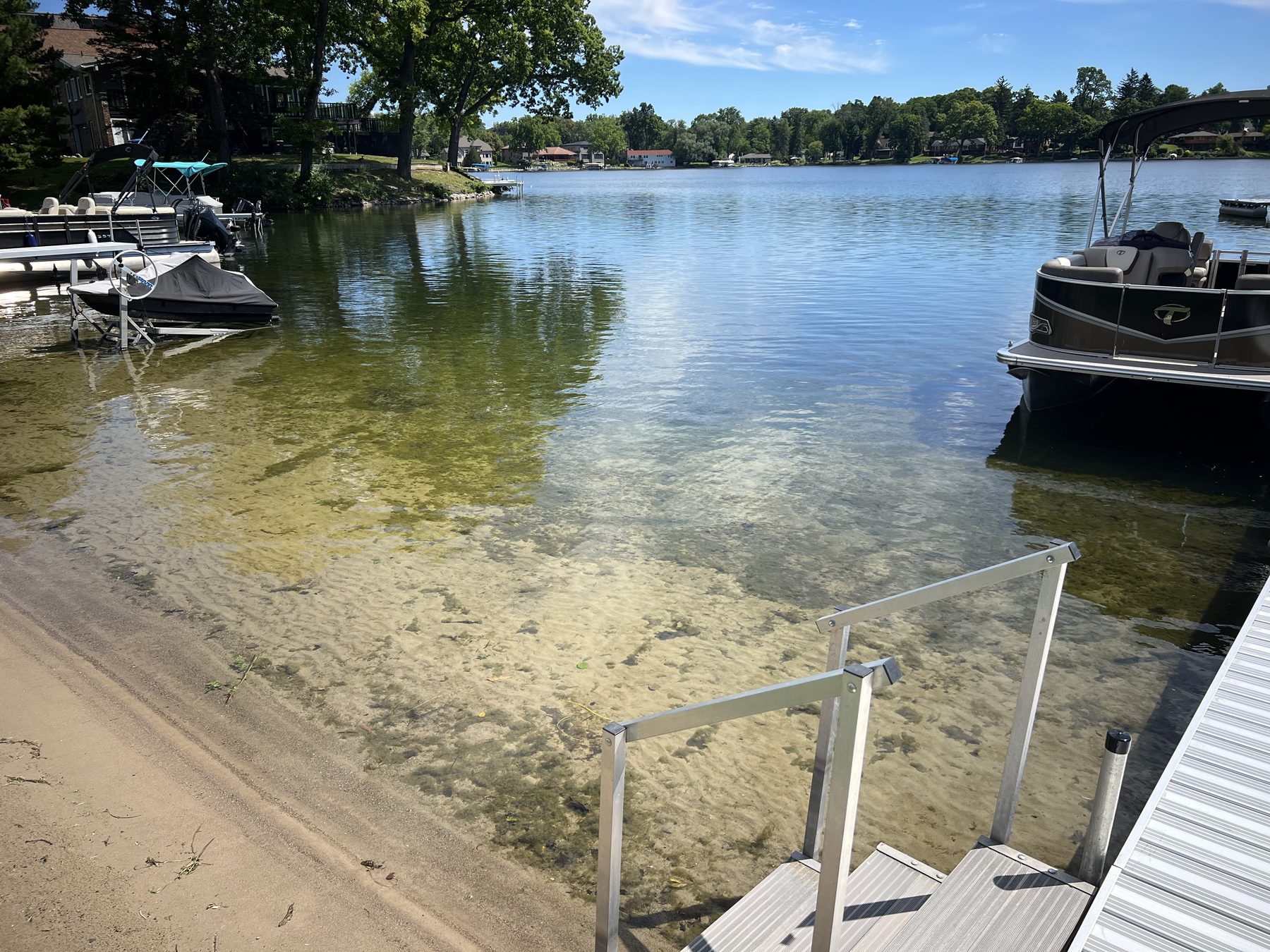 Lake-lot beach, dock, and pontoon boats on a clear day