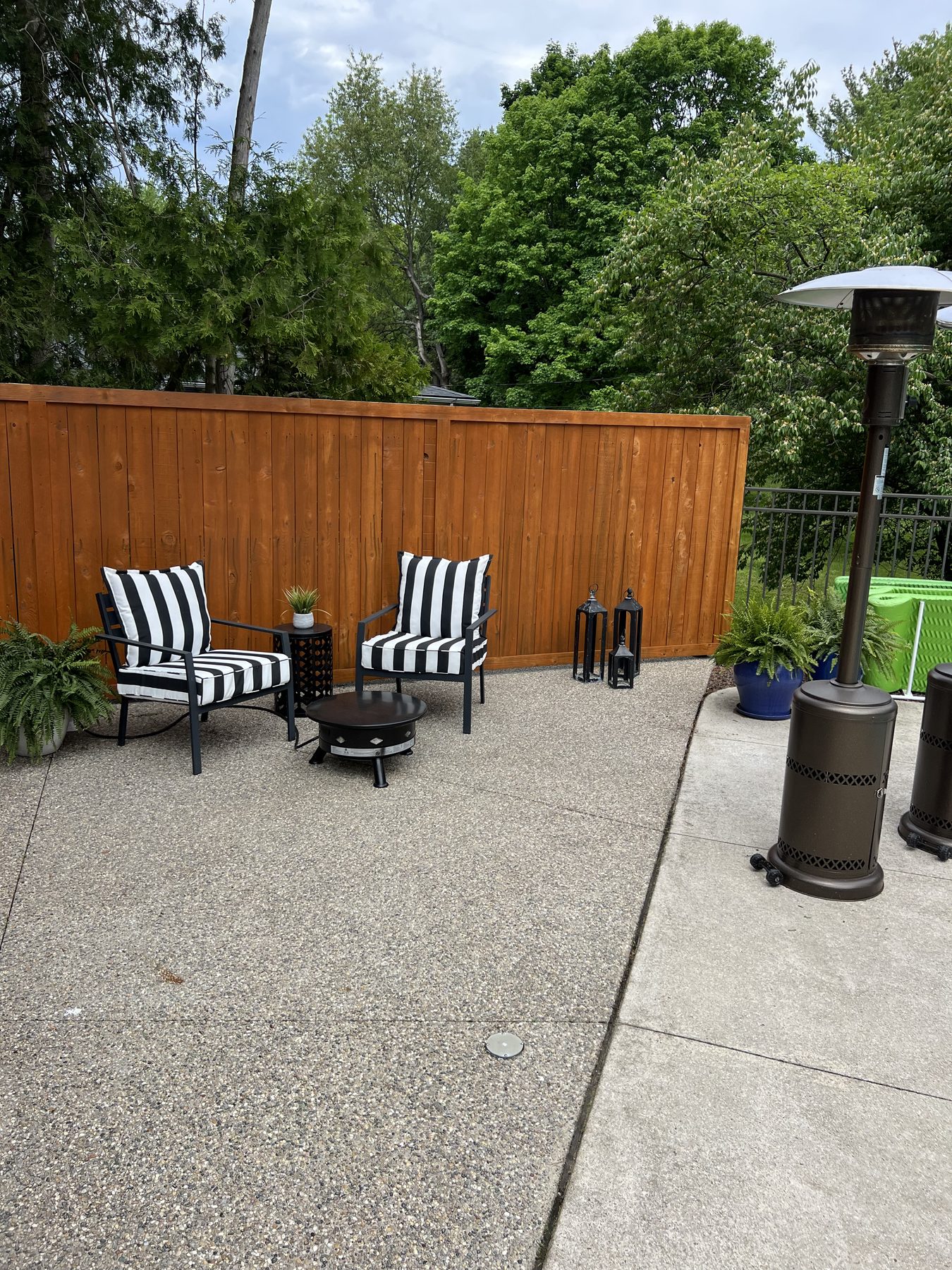 Seating nook on a concrete patio against a wood fence, with potted ferns