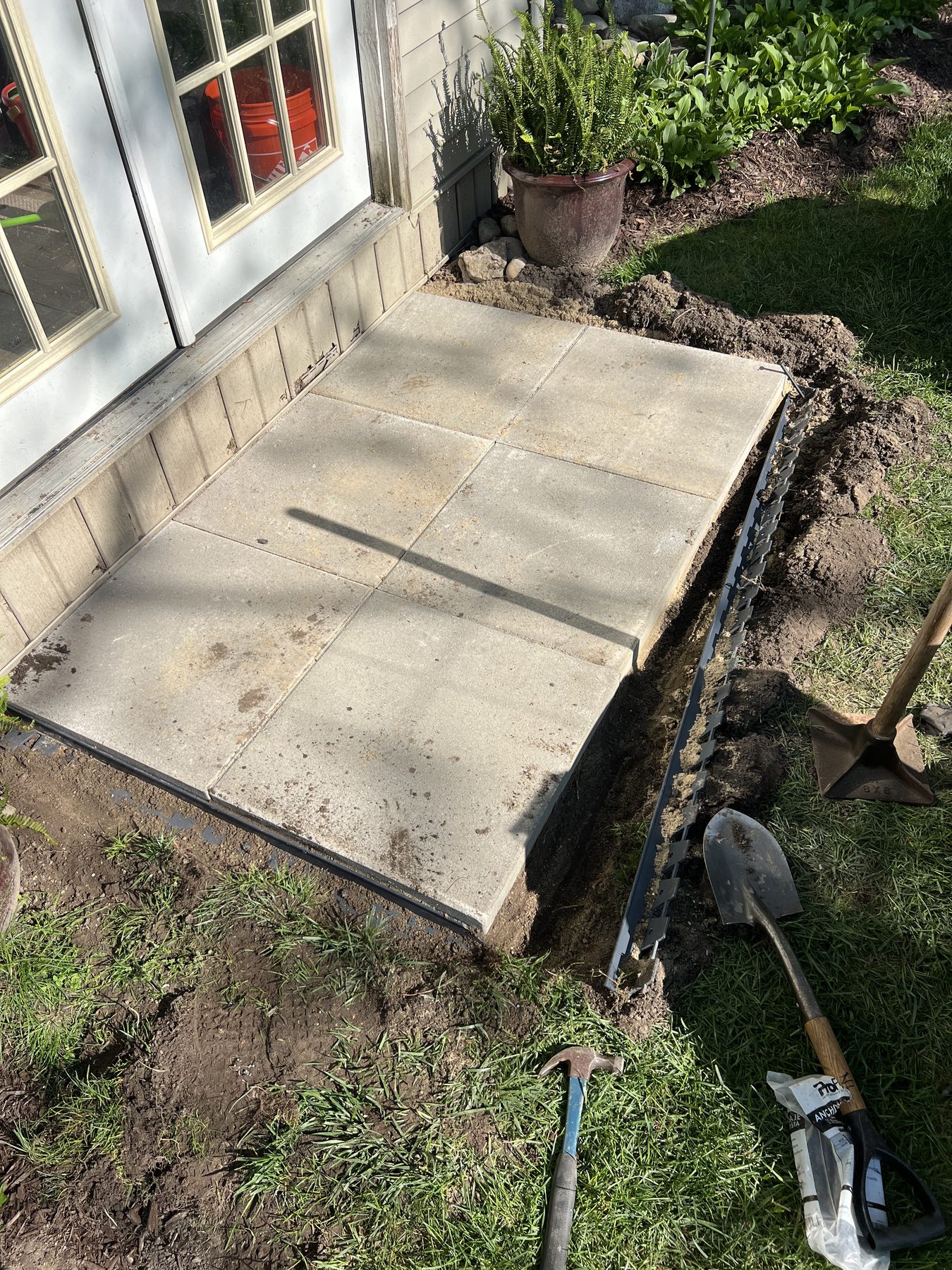 Concrete paver landing being set by a back door, with edging and a shovel