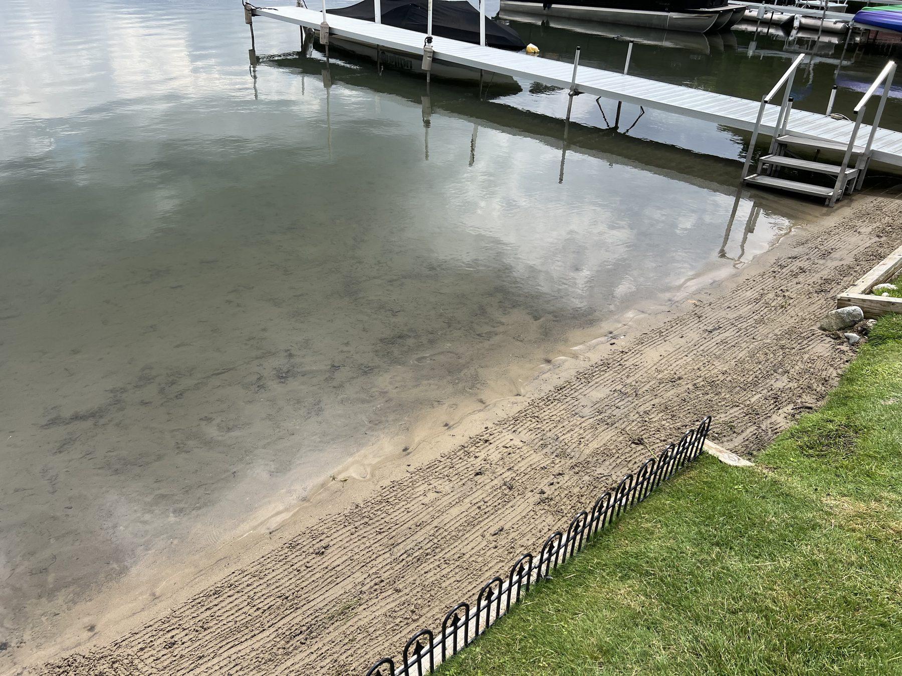 Sandy shoreline with rake marks between the grass and the dock